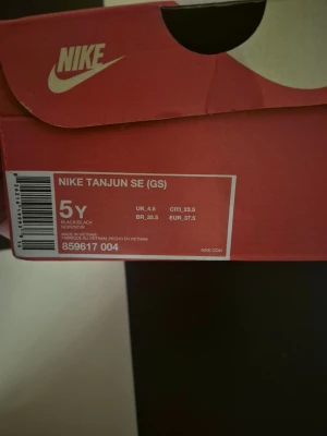 Nike Tanjun SE svarta sneakers med glitter - Nike Tanjun SE sneakers i helsvart med diskret glittrig finish. Skorna har en klassisk låg siluett, svart Nike-logga på sidan och ovandel i textil för en lätt och luftig känsla. Perfekta för dig som gillar stilrena och bekväma sneakers.