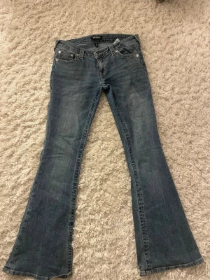 True Religion bootcut jeans blå, stl 28 - Säljer ett par klassiska blå jeans från True Religion i modell med bootcut. Snygga kontrastsömmar och ikoniska bakfickor med broderad logga. Jeansen är väldigt lågmidjade. Men behöver tyvärr sälja för att de är för stora för mig.  Jensen är lite trampade på i slutet, finns en blid. Köpte jeansen för 1200 och säljer för 850. 