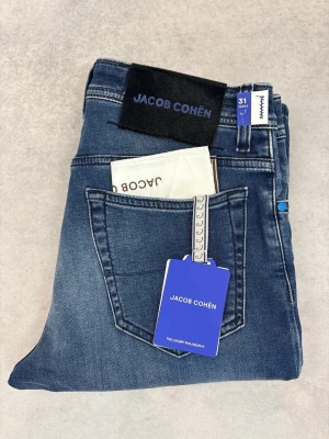 Blå jeans från Jacob Cohën - Snygga blå jeans från Jacob Cohën med klassisk femficksmodell och raka ben. Jeansen har en tvättad finish med lätt slitning på låren och en svart patch med logga bak. Tillverkade i mjukt denimtyg för skön passform.