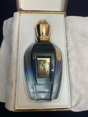 Xerjoff Torino21 parfym - Lyxig parfym från Xerjoff i modellen Torino21. Flaskan är elegant med en gradient i blått och svart, dekorerad med guldfärgade detaljer och lock. Kommer i exklusiv presentförpackning med vit insida och guldfärgade kanter. Perfekt för dig som gillar exklusiva dofter.