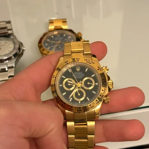 Herrklocka  - Exklusiv herrklocka helguld med svart urtavla och guldiga detaljer. Klockan har kronograf-funktion och klassisk länkarmband i metall. Perfekt för dig som gillar lyxig och tidlös design.