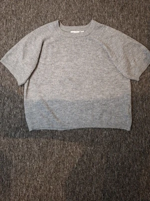 Grå stickad tröja från 157 - Säljer en enkel och stilren grå stickad tröja från 157 med korta ärmar och rund hals. Tröjan har en rak passform och är gjord i mjukt stickat material som passar perfekt till vardagslooken.