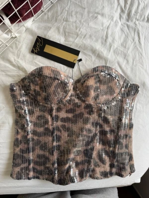 Leopardmönstrad paljettkorsett - Supersnygg leopardmönstrad korsettopp från Ambisu med paljettdetaljer, köpt på NewYorker. Toppen är axelbandslös och har vadderade kupor för extra stöd. Materialet är glittrigt och ger en riktigt trendig look. Perfekt för dig som vill sticka ut och älskar djurmönster!