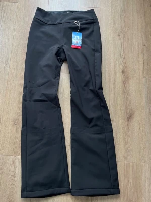 Svarta skidbyxor från Helly Hansen - Säljer ett par svarta skidbyxor från Helly Hansen med utsvängda ben och hög midja. Byxorna är tillverkade i ett slitstarkt, vattenavvisande material och har diskret HH-logga på benet och baktill. Perfekta för kalla dagar i backen eller utomhusaktiviteter. Helt nya med lapp kvar! 