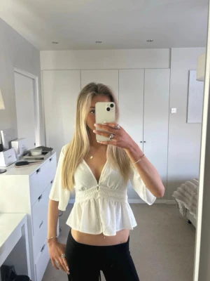 Vit v-ringad blus med volang - Snygg vit blus med v-ringning och knappar framtill. Blusen har volang nertill och trekvartsärmar. Tillverkad i ett lätt och luftigt material, perfekt för varmare dagar. Passar till både jeans och kjol för en trendig look.