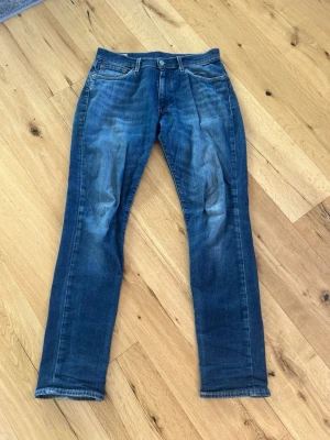 Levi's 511 blå jeans herr - Säljer ett par klassiska Levi's 511 jeans i blå denim med snyggt slitna detaljer och raka ben. Jeansen har fem fickor, knappgylf och är tillverkade i bomull med lite stretch för extra komfort. Perfekta för en avslappnad och trendig look.