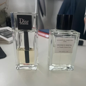 Dior Homme Sport parfym & Orange x Santal - Två exklusiva parfymer: Dior Homme Sport i en stilren, transparent glasflaska med svart lock och Essential Parfums Orange x Santal i en elegant, fyrkantig flaska med svart lock. Båda har minimalistisk design och tydliga etiketter.