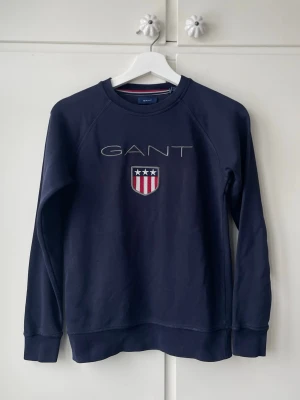 Mörkblå sweatshirt från GANT - Marinblå GANT-tröja i storlek 146–152, men sitter som en XS. Klassisk modell med broderad logga framtill. Mycket bra skick, inga fläckar eller skador.  Snabb leverans. Skriv gärna vid frågor!