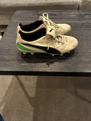 Puma King Finale Green FG - Säljer ett par klassiska Puma King fotbollsskor i beige med svarta och gröna detaljer. Skorna har snörning, svart Puma-logga på sidan och gröna inslag på sulan. Ovandelen är i läder och skon har dobbar för spel på gräs. Är originellt dam skor men hade dom som kille med storlek 38-39 och dom var supersköna. Perfekt om man vill ha ett par riktigt unika skor.