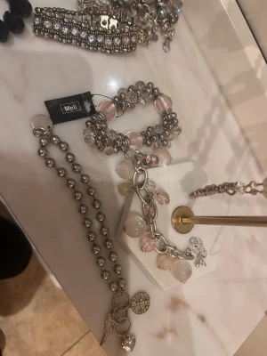 Silverfärgat armband med pärlor - Snyggt armband från Meli i silverfärg med stora länkar och hängande pärlor i rosa och vitt. Armbandet har en modern design med mix av metall och glaspärlor som ger en cool och trendig look. Perfekt accessoar för att lyfta din outfit.