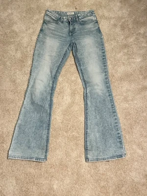 Ljusblå bootcut jeans från Lindex - Säljer ett par ljusblå bootcut jeans från Lindex, modell Freja. Jeansen har klassisk femficksdesign, normalhög midja och snygg tvättad look. Perfekta för dig som gillar retrovibbar och vill ha ett par bekväma jeans med lite utsvängda ben.