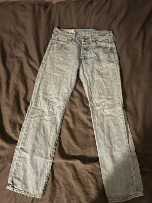Levi's ljusblå raka jeans - Säljer ett par klassiska ljusblå Levi's jeans med rak passform och fem fickor. Jeansen har en vintagekänsla med den ikoniska läderlappen bak i midjan och röda Levi's-taggen på bakfickan. Tillverkade i slitstark denim, perfekta för en avslappnad look.