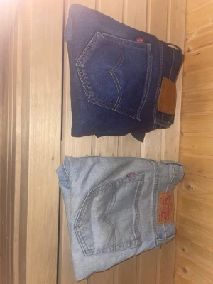 Levi's 514 jeans bootcut blå & Levi’s 515 ljusblå - Två par Levi's 514 jeans, ett par i mörkblå denim och ett par i ljusblå denim. Klassisk femficksmodell med Levi's ikoniska läderpatch bak och röd logga vid bakfickan. Bootcut passform på de mörkare och slim taper på de ljusare. Båda är i W32 L32