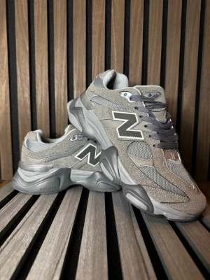 Grå New Balance 9060 sneakers - Snygga grå New Balance 9060 sneakers med chunky sula och ikoniska N-loggan på sidan. Ovandelen är i mesh och mocka för en sportig vibe. Skorna har gråa skosnören och detaljer i olika nyanser av grått. Perfekta för dig som gillar streetwear och vill ha något bekvämt och stilrent.