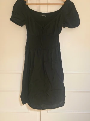 Svart kort klänning med puffärm - Söt svart kort klänning från Bik Bok med puffärmar och smockad midja. Klänningen har en lätt v-ringning med knyt framtill och är tillverkad i ett mjukt bomullstyg. Även knyte vid bröst och ribbad under bröst