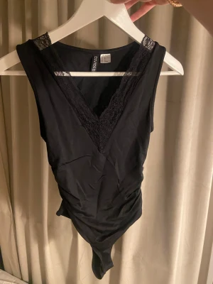 Svart body med spets från H&M - Svart bodysuit från H&M divided med v-ringning och spets. Storlek Xs. Aldrig använd 