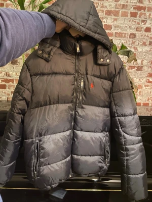 Svart pufferjacka från Ralph Lauren - Jag säljer denna polo Ralph lauren jacka eftersom att den inte var vad jag tänkte mig.   Kunde inte skicka tillbaka den så jag försöker sälja av den här istället för att kunna få tillbaka lite av pengarna iallafall.  OBS: den har en liten fläck på ryggen och ”handtaget” på dragkedjan är sönder men det kan med högsta trolighet fixas hos en skräddare, har även en liten skråma på ryggen som nästan är osynlig  Om du har några frågor om varan så tveka inte på att skriva till mig😊 (nypris runt 3500kr)