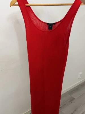 Röd ribbad långklänning Linex - Snygg röd långklänning från Linex med ribbad struktur. Klänningen är ärmlös och har en rund halsringning. Perfekt för dig som vill ha en enkel men stilren look.