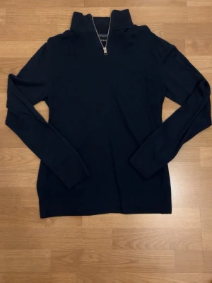 Mörkblå halvzip tröja - Det här är en stilren quarter zip tröja från Jack & Jones. Tröjan har inga slitningar och sitter perfekt på kroppen. Ingen del av tröjan sitter konstigt eller är ut töjd. Den inte super tjock i material vilket gör den väldigt lätt och bekväm att ha på sig. Materialet ger helt enkelt en känsla av bra kvalitet. Jag har inte använt tröjan mycket alls. Hör av dig vid minsta intresse samt frågor!