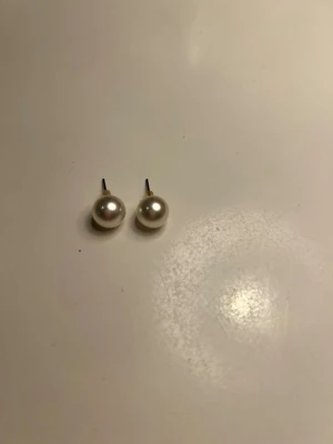 Klassiska pärlörhängen i silver - Säljer ett par stilrena pärlörhängen med rund form och vit skimrande yta. Stiftet är i silverfärg och örhängena har en tidlös look som passar till många stilar. Perfekta för dig som gillar enkel men elegant design.