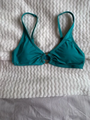 Turkos bikiniöverdel med ringdetalj - Snygg turkos bikiniöverdel med trekantsformade kupor och en cool ringdetalj framtill. Justerbara axelband för perfekt passform. Perfekt för lata dagar på stranden eller poolen.