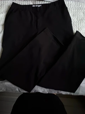 Svarta kostymbyxor från NA-KD - Säljer ett par klassiska svarta kostymbyxor från NA-KD. Byxorna har rak passform och hög midja, perfekta för en clean och stilren look. Materialet känns mjukt och följsamt, vilket gör dem bekväma att bära hela dagen.