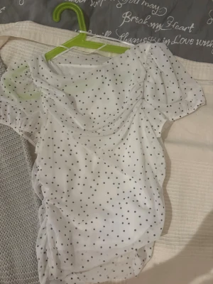 Vit prickig blus från H&M - Söt vit blus från H&M med svarta prickar och puffiga korta ärmar. Blusen har en draperad framsida och är gjord i ett tunt, lätt material som ger en luftig känsla. Perfekt för en trendig och avslappnad look.