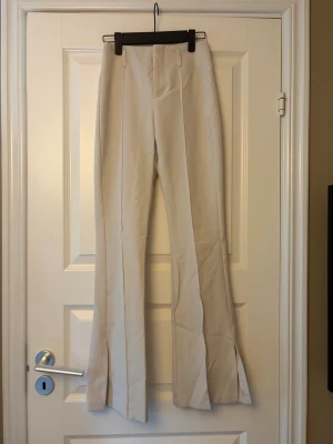 Kostrymbyxor  - Beige/vita kostrymbyxor från Bershka som är utsvängda och har en liten slits nere på benet. Storlek 32 och passar dig som är ca 165cm. Pris går alltid att diskutera.