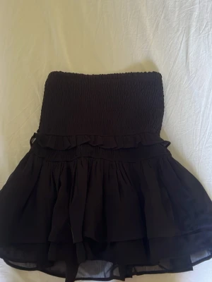 Svart volangkjol från Gina Tricot - Supersöt svart kortkjol från Gina Tricot med smock i midjan och flera lager volanger. Kjolen har en luftig och flowy känsla, perfekt för att styla med crop tops eller stickade tröjor. Tillverkad i ett lätt syntetmaterial.