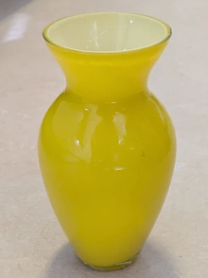 Gul vas i glas med rund form - Säljer en snygg vas i glas med klargul färg och rundad form. Vasen har en bred öppning upptill och smal midja, perfekt som dekoration eller för blommor. Enkel men stilren design som lyser upp rummet. På sista bilden finns en bild på en liten skada 
