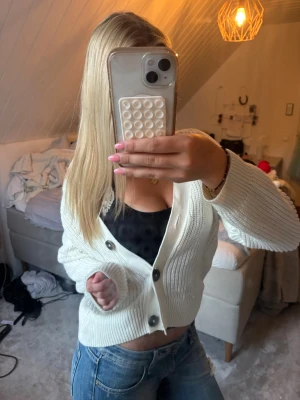 Vit ribbad kofta från Lindex - Säljer en vit ribbad kofta från Lindex med stora bruna knappar framtill. Koftan har en croppad passform och långa ärmar. Perfekt att slänga över ett linne eller t-shirt för en chill look.