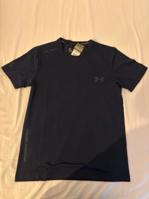 Under Armour träningsset – T-shirt + shorts - Säljer ett snyggt och funktionellt träningsset från Under Armour. Setet består av en snabbtorkande T-shirt och matchande shorts med resår och dragsko i midjan. Perfekt för gym, löpning, padel eller annan träning.  ✔️ Storlek: M ✔️ Skick: Helt nytt med prislappar kvar ✔️ Färg: Svart ✔️ Lätt, ventilerande och bekvämt material  Säljs som set. Hör gärna av dig om du har frågor eller vill ha fler bilder!