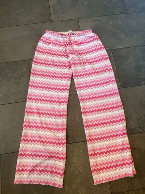 Gina tricot Zigzag  - Mysiga pyjamasbyxor i bomull med rosa och vita zigzag-ränder. Byxorna har resår i midjan och dragsko för skön passform. Perfekta för chillkvällar hemma eller när du vill vara extra bekväm. Säljer pga köpt ett par andra, helt slutsålda i butik därav pris. 