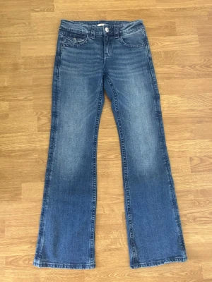 Blå bootcut jeans med broderade fickor - Blåa bootcut jeans lågmidjade från gina tricot. Detaljer på fickorna på baksidan med knappar. Aldrig använt. Skickas inom 1-2 dagar.