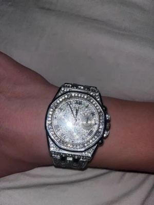 Glittrig ap inspererad silverfärgad klocka - Säljer en riktigt blingig klocka i silverfärg med massor av glittrande kristaller på både urtavlan och armbandet med inga extra likns. Klockan har en klassisk rund form och länkarmband i metall. Perfekt för dig som vill sticka ut och gillar accessoarer som syns. Den är ganska liten