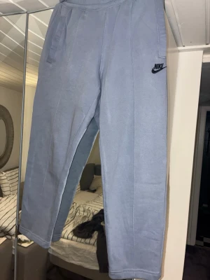 Ljusblå/grå mjukisbyxor från Nike - Säljer ett par ljusgrå mjukisbyxor från Nike med broderad svart logga på vänster sida. Byxorna har raka ben, resår i midjan och praktiska sidofickor. Tillverkade i mjukt och bekvämt material, perfekta för chill dagar eller träning. Till för Män men kan även passa kvinnor 