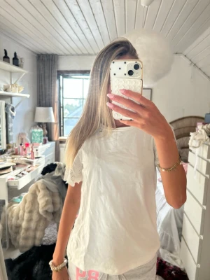 Vit topp med broderade spetsärmar - Säljer en söt vit topp med korta ärmar i broderad spets och rund halsringning. Toppen har en avslappnad passform och är gjord i ett lätt bomullstyg. Perfekt för dig som gillar en enkel men ändå detaljerad stil.
