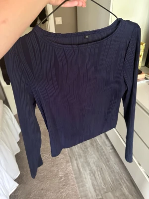 Mörkblå ribbad långärmad topp - Snygg mörkblå långärmad topp med ribbad struktur och rund halsringning. Perfekt att styla med jeans eller kjol för en trendig look. Toppen har en slim passform och är superenkel att matcha med olika outfits.