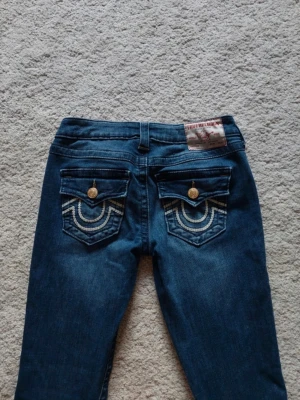 Mörkblå True Religion Jeans - Säljer pga att de inte används. Dem är i storlek w25, modell Joey. Jag har sytt upp byxorna så dem ska passa mig i längden då dem är precis ner till golvet för mig som är 164. De passar även om man skulle va 159-166 ish. Men om man skulle vilja är det jätte enkelt att fålla ner igen! Jag har även sytt in dom i midjan ett par gånger (se bild 6,7) men jag har tagit bort det nu och sytt igen hålen, och det är inget som syns när byxorna är på, utan de är bara på insidan och de är inget man märker!