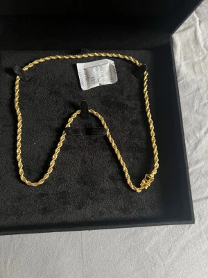 Guld pläterat 18k - Snyggt guldfärgat halsband med tvinnad kedja och elegant lås. Halsbandet har en klassisk design som passar till många olika stilar. Tillverkat i metall med glansig finish och levereras i en svart ask.