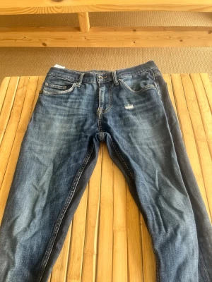Blå Tiger of Sweden jeans - Snygga blå jeans från Tiger of Sweden med klassisk femficksmodell och slitningar framtill. Jeansen har en rak passform och är tillverkade i ett mjukt denimtyg. Perfekta för en avslappnad och trendig look. Har hål men som inte visar något tecken av hud, men istället har hål vid fickan men går inte igenom eller har några risker att saker ska falla ut!