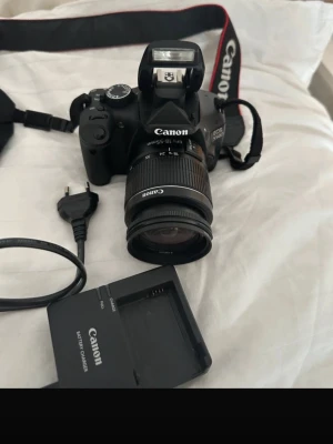 Canon EOS 550D systemkamera med objektiv - Canon EOS 550D systemkamera i svart med tillhörande 18-55mm objektiv. Kameran har en stor LCD-skärm, inbyggd blixt och tydliga reglage. Rem, batteriladdare och strömkabel ingår. Perfekt för dig som vill ta snygga bilder och utveckla ditt fotograferande.