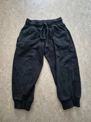 Mjukisbyxor - Svart mjukisbyxor med resår i midjan och dragsko för skön passform. Byxorna har ribbade muddar vid bensluten och två sidofickor. Tillverkade i mjukt bomullsmaterial som är perfekt för chill dagar. Har hål.