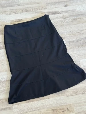 Svart långkjol från Betty Barclay - Klassisk svart långkjol från Betty Barclay med diskreta sömdetaljer. Kjolen har en enkel och stilren design, perfekt för dig som gillar minimalistiskt mode. Tillverkad i ett mjukt och följsamt material som ger en snygg siluett.