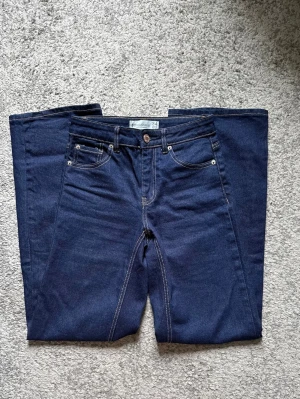 Mörkblå raka jeans från Stradivarius - Säljer ett par mörkblå jeans med raka ben och klassisk femficksmodell. Jeansen har kontrastsömmar och normalhög midja. Tillverkade i ett mjukt denimtyg som ger en skön känsla. Perfekta till din vardagsstil!