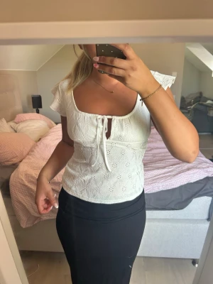 Vit blus med knyt och volangärm - Söt vit blus med broderade detaljer, knyt framtill och volangärmar. Toppen har en feminin v-ringning och är figurnära i modellen. Perfekt för dig som gillar romantisk och trendig stil.