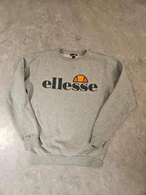 Grå sweatshirt från Ellesse - Snygg grå sweatshirt från Ellesse. Tröjan har rund halsringning, långa ärmar och ribbade muddar vid ärmslut och nederkant. Perfekt för en avslappnad och sportig stil. Väldigt fint skick!