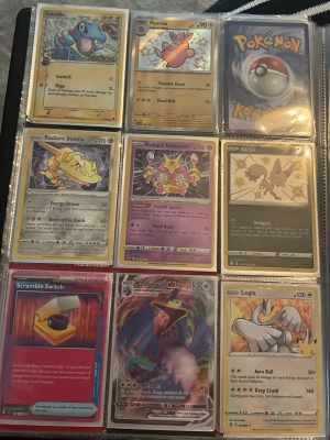 Pokémonkort i samlarpärm - Samling med Pokémonkort i en plastpärm, innehåller bland annat Totodile, Pawmo, Radiant Steelix, Radiant Alakazam, Nickit, Scramble Switch, Garchomp Vmax och Lugia. Korten har färgstarka illustrationer och varierande design. Perfekt för dig som gillar Pokémon och samlarkort.
