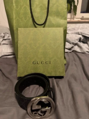 Svart GG Supreme bälte från Gucci - Snyggt svart bälte från Gucci med GG Supreme-mönster och en stor, rund silverspänne med dubbla G-loggan. Bältet är gjort i skinn och har en stilren och modern look som lyfter vilken outfit som helst.  Låda och Gucci ”kartong/påse” medföljs och kvitto! Original pris 4800kr.               Snabb affär 1000kr