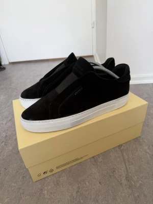 Svarta sneakers från Axel Arigato - Stilrena svarta sneakers från Axel Arigato i mocka med vit, chunky sula. Minimalistisk design utan synliga snören och diskret logga på sidan. Perfekta för dig som gillar en clean och modern look. Skorna har nyligen rengjorts proffesionellt så de är intill nya!